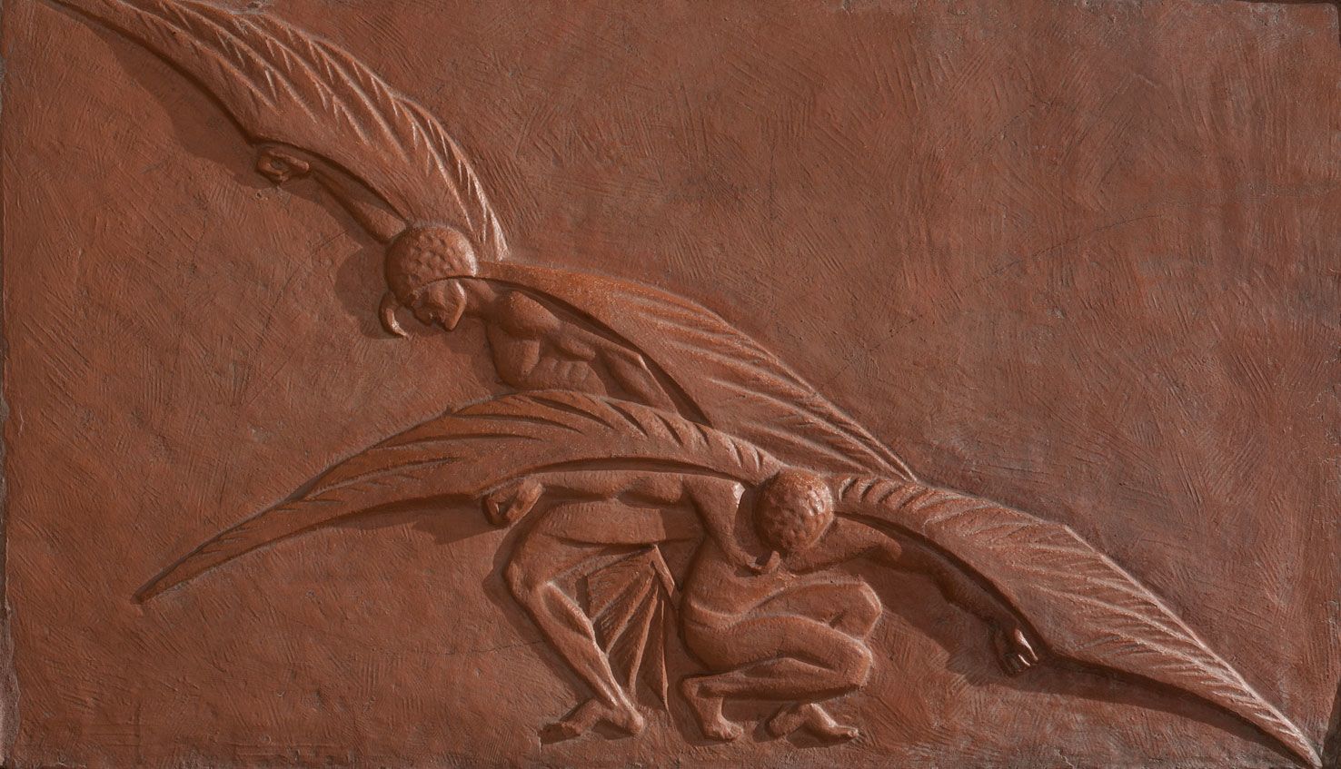 This terracotta relief sculpture depicts two muscular winged figures crouching against a reddish, textured background.