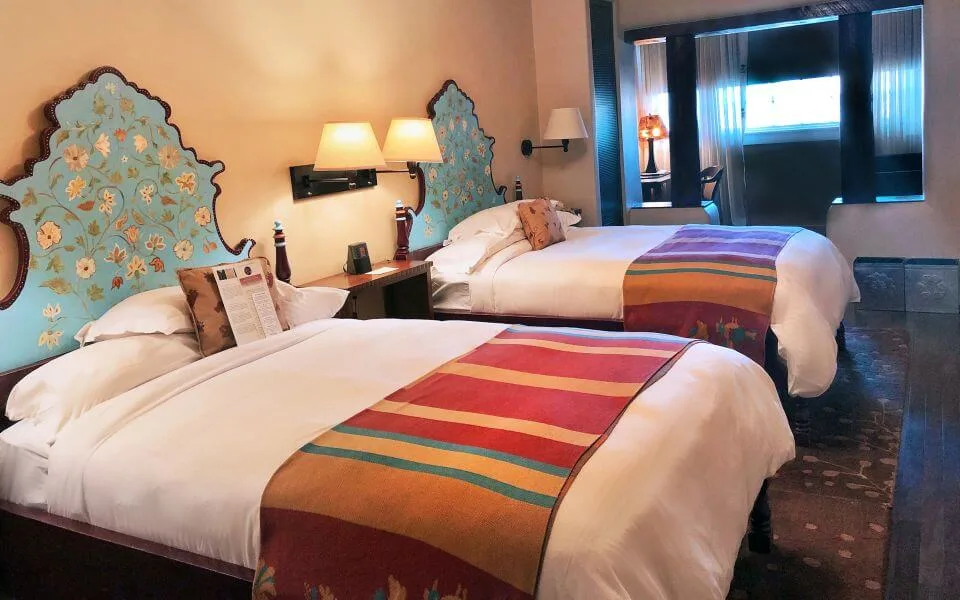 Two comfortable hotel rooms with hand-painted floral headboards and colorful striped bed runners.