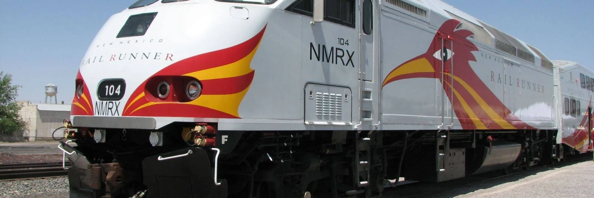 A white and gray commuter train engine with distinctive red and yellow graphics is waiting at the station.