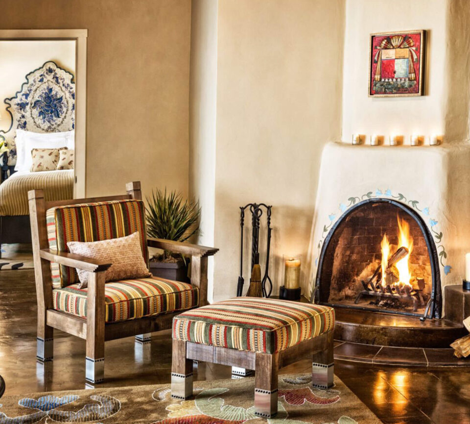 A cozy, striped armchair and ottoman are positioned beside a warm, lit adobe fireplace.