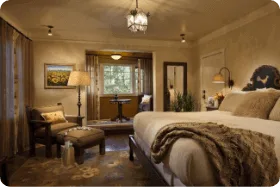 A beautiful and spacious hotel room features a king bed, warm lighting, and an armchair next to a window nook.