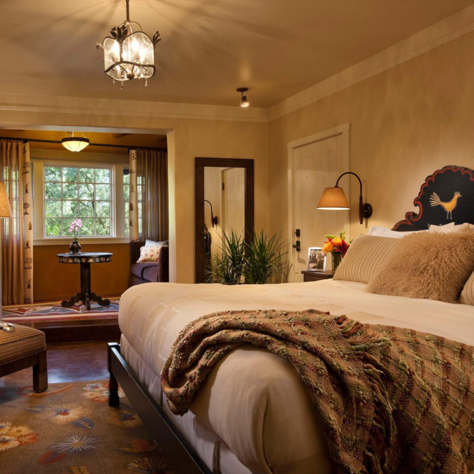 This cozy hotel room features a large bed with a decorative, carved headboard, Southwestern textiles, and a sunlit.