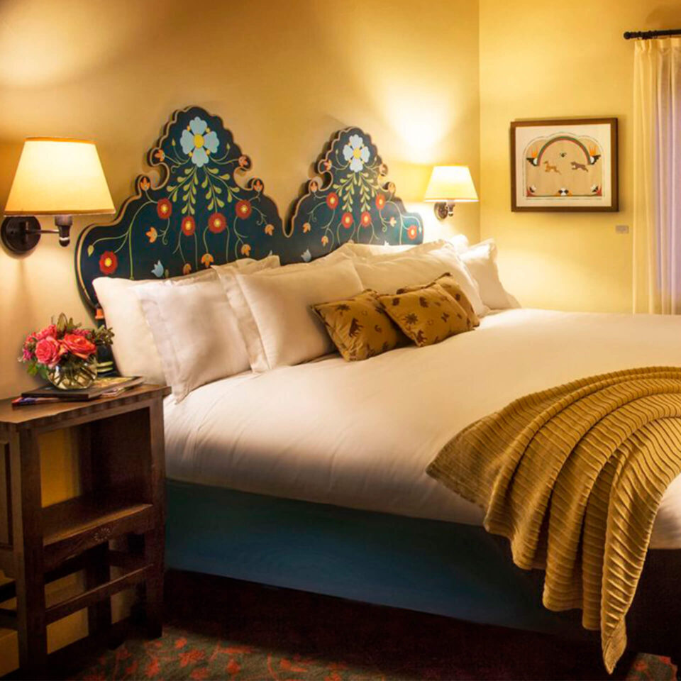 This Santa Fe hotel room showcases a richly decorated, custom-made floral headboard and comfortable white bedding.