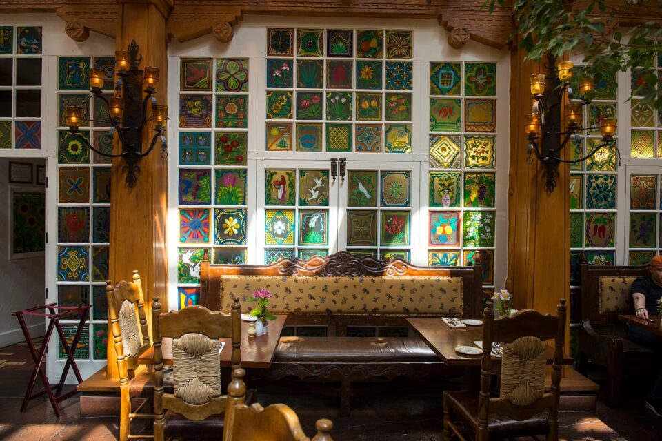 Guests enjoy comfortable wooden seating near the decorative painted windows of the restaurant.