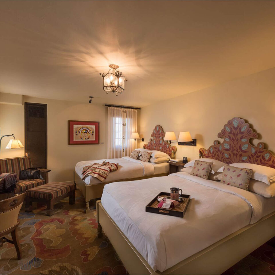 A warm and inviting boutique hotel room featuring two double beds with artistic, painted headboards and a plush.