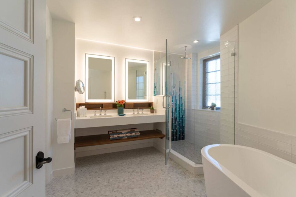 The bright, modern hotel rooms bathroom features a double vanity, separate glass shower, and freestanding tub.