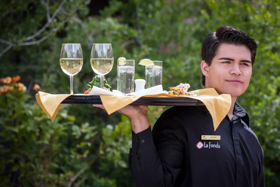 A hotel staff member delivers wine and water on a tray for excellent service at our restaurants.