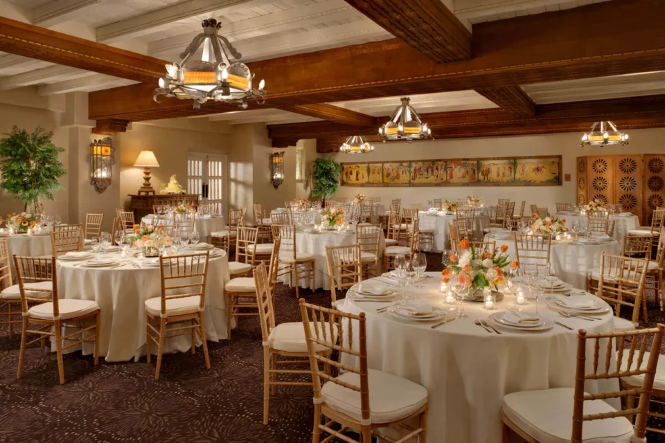 The elegant banquet hall is set for a formal event featuring wooden ceiling beams, white-draped tables, and floral.