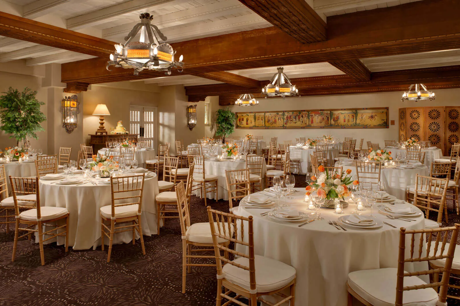 The elegant banquet hall is set for a formal event featuring wooden ceiling beams, white-draped tables, and floral.