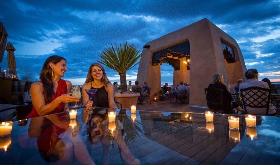 Guests enjoy cocktails and conversation on the candlelit outdoor rooftop bar patio at dusk.