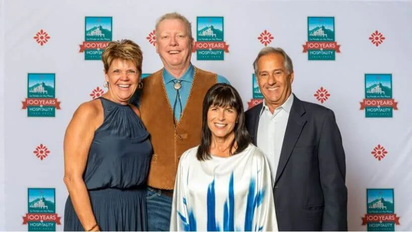 Four smiling guests pose together against the anniversary backdrop celebrating a century of hospitality.