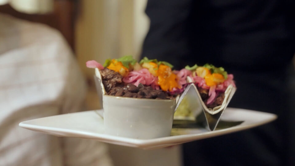 A waiter serves two colorful gourmet tacos and black beans on a white plate at the downtown Santa Fe restaurant.