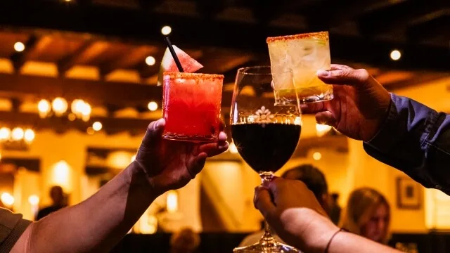 Three guests raise glasses of colorful margaritas and wine in a celebratory toast at the downtown bar.