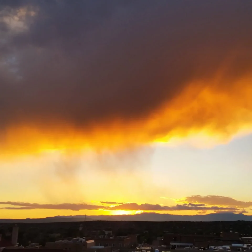 The cityscape is silhouetted against a dramatic sunset where dark clouds are intensely illuminated in orange and yellow.