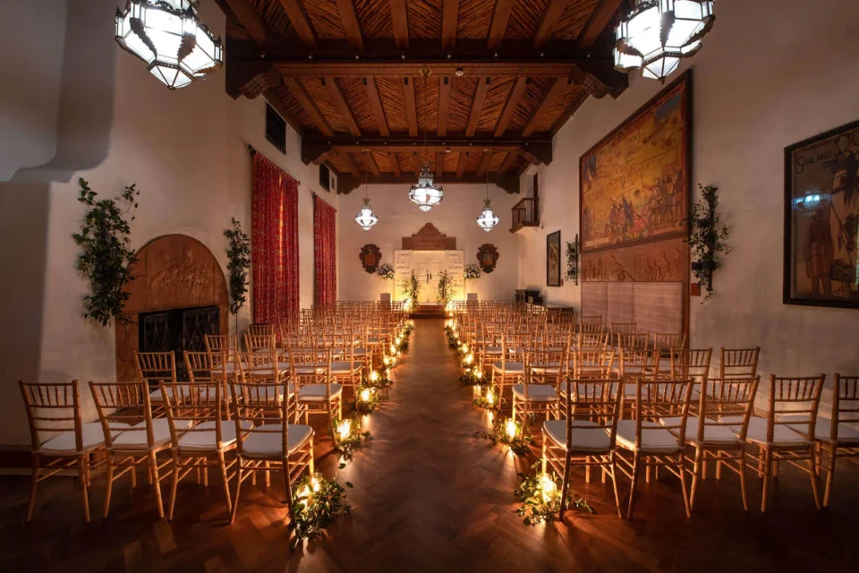 This beautiful event space is set up for a wedding ceremony with chairs lining the candlelit aisle.