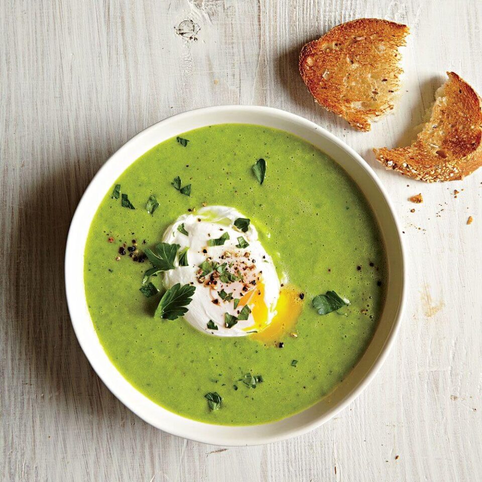 A close-up view of vibrant green soup topped with a creamy poached egg and two pieces of toasted bread.