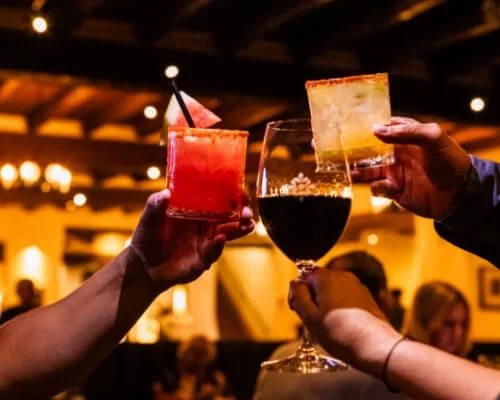 Guests toast with colorful specialty cocktails and red wine in the warm ambiance of a downtown restaurant.