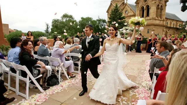 The bride and groom joyfully exit their ceremony as guests throw pink flower petals on the beautiful outdoor wedding.