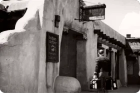 A sepia-toned photograph depicts a traveler carrying luggage toward the historic downtown santa fe hotels entrance.