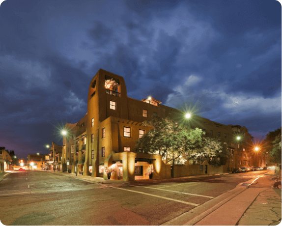 The beautifully illuminated adobe exterior showcases classic architecture of a santa fe boutique hotel.