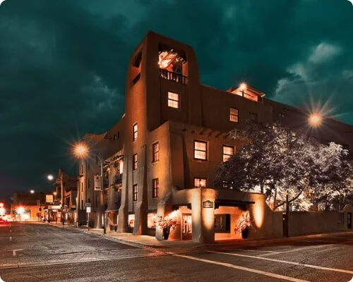 The historic adobe boutique hotel glows warmly at night along the street corner.