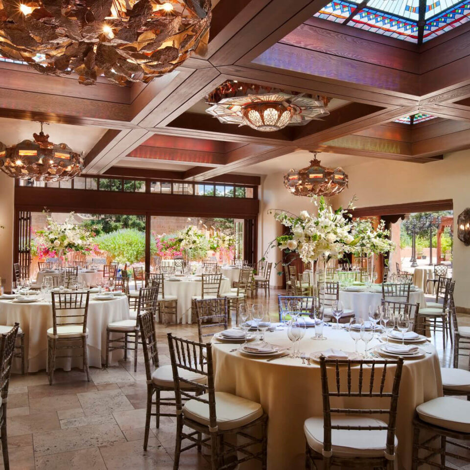 This luxurious banquet hall is set with tables, unique chandeliers, and opens onto a flower-filled patio.