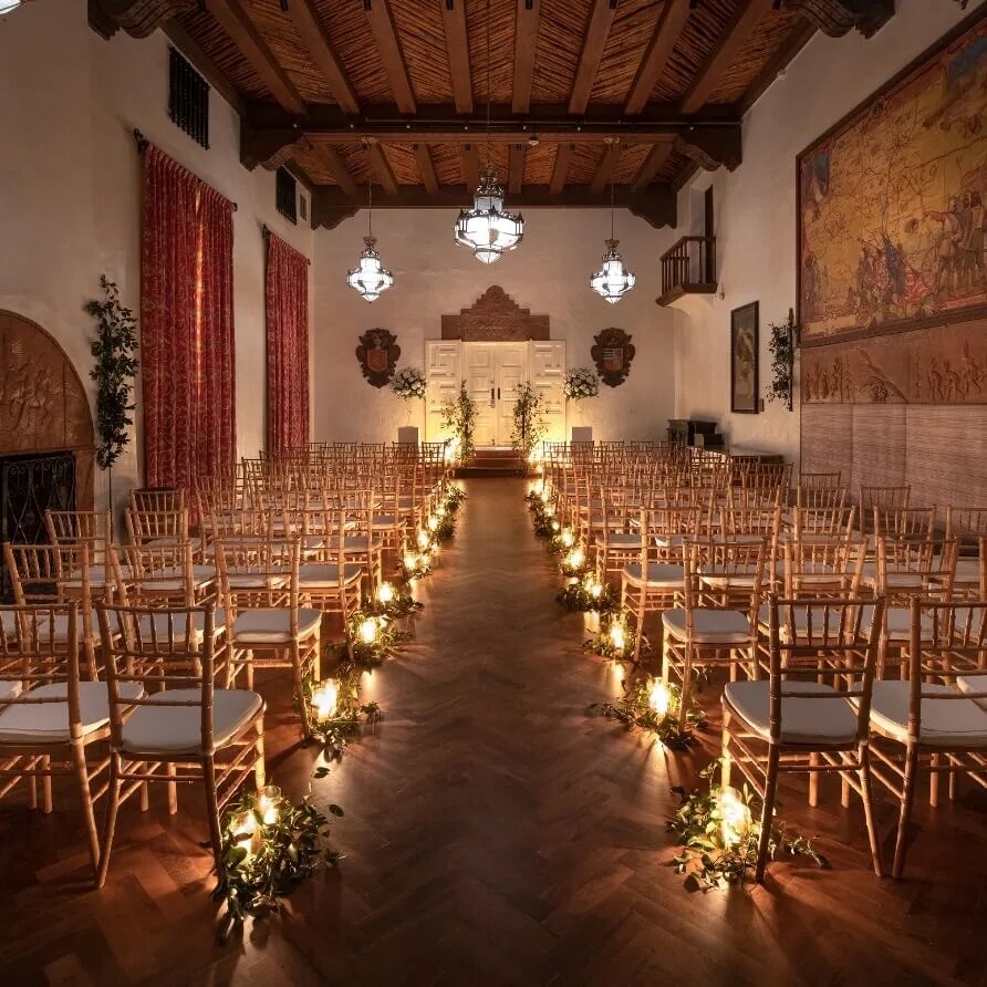 The large ballroom is configured as a wedding venue with a candlelit aisle, wooden beam ceilings, and antique.