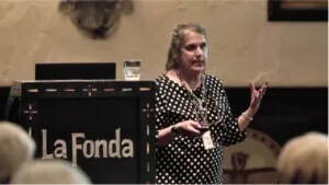 A female speaker addresses an audience from a dark lectern in one of the professional event spaces.