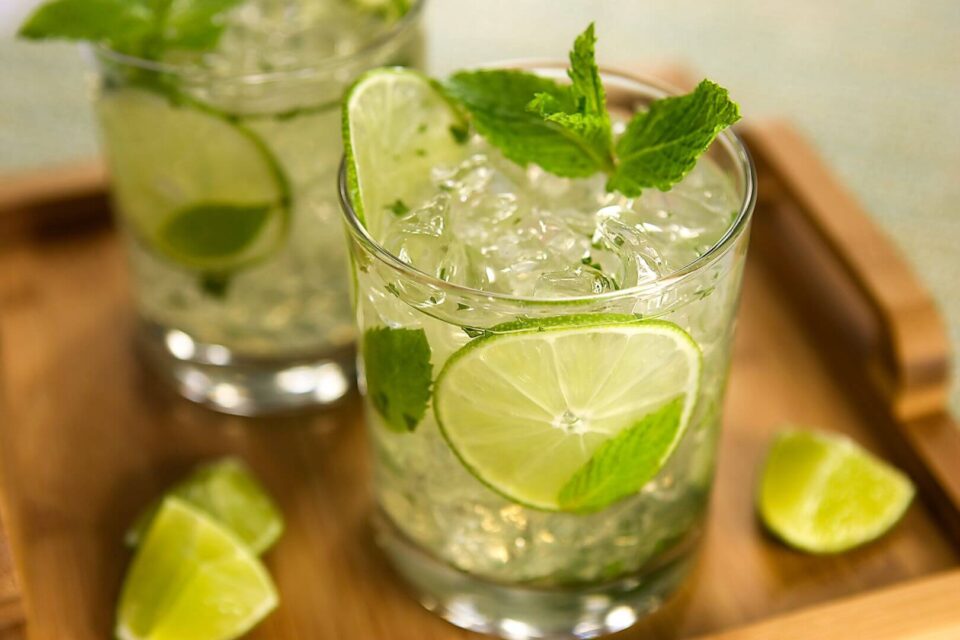 Two crushed ice cocktails garnished with fresh lime and mint are served on a wooden tray, perfect for the rooftop bar.
