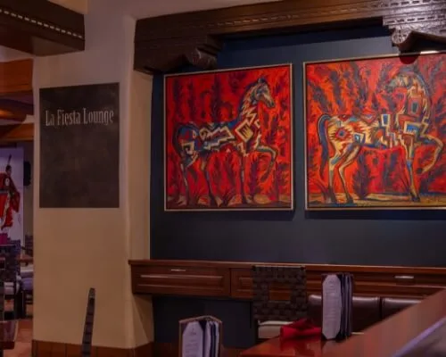 The inviting interior of this lounge, one of the downtown Santa Fe restaurants, displays vibrant artwork and cozy booth.