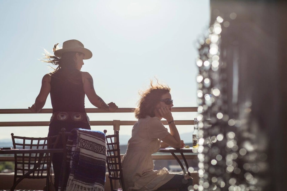 Two people enjoying a drink and the sunny view from the hotel's rooftop bar and patio.