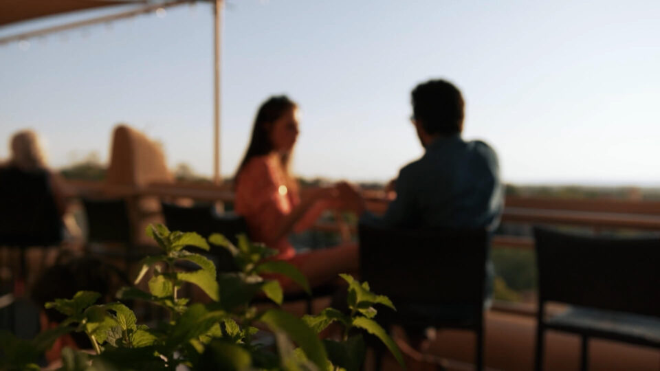 A couple enjoys drinks and conversation on a scenic rooftop bar patio at sunset.