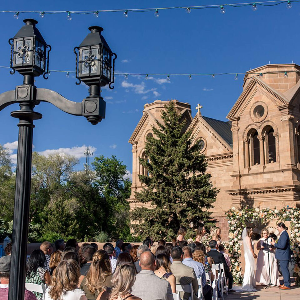Guests watch a couple exchange vows at an elegant outdoor wedding venue set against a historic stone building.