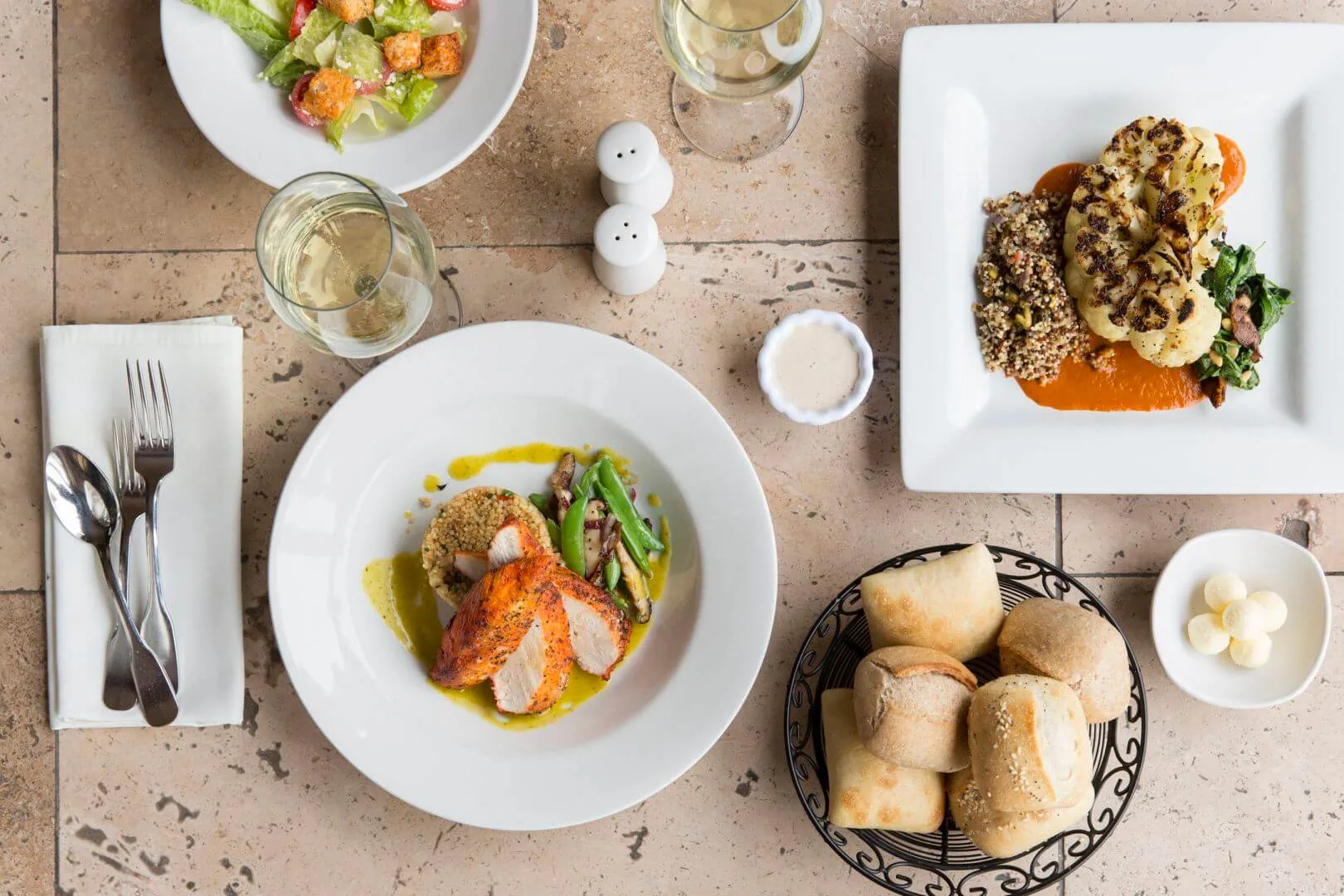 A table set with various dishes of food, including plates of meat and vegetables, bread, and glasses of wine.
