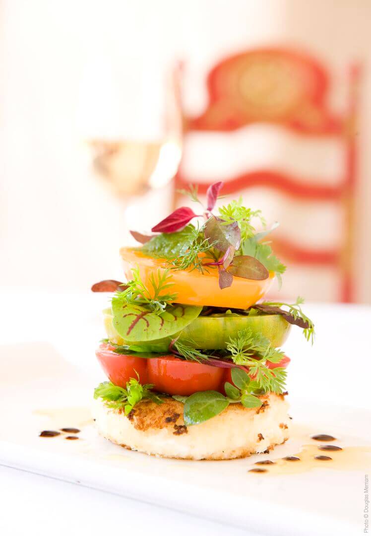 An elegantly plated tower of heirloom tomatoes, fresh greens, and seared cheese is served on a white dish at the.
