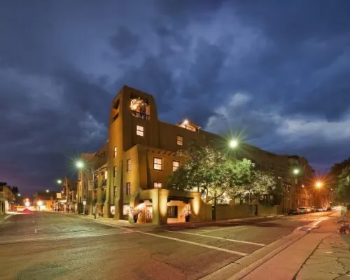 The large Pueblo Revival boutique hotel stands lit up at night on a prominent downtown street corner.
