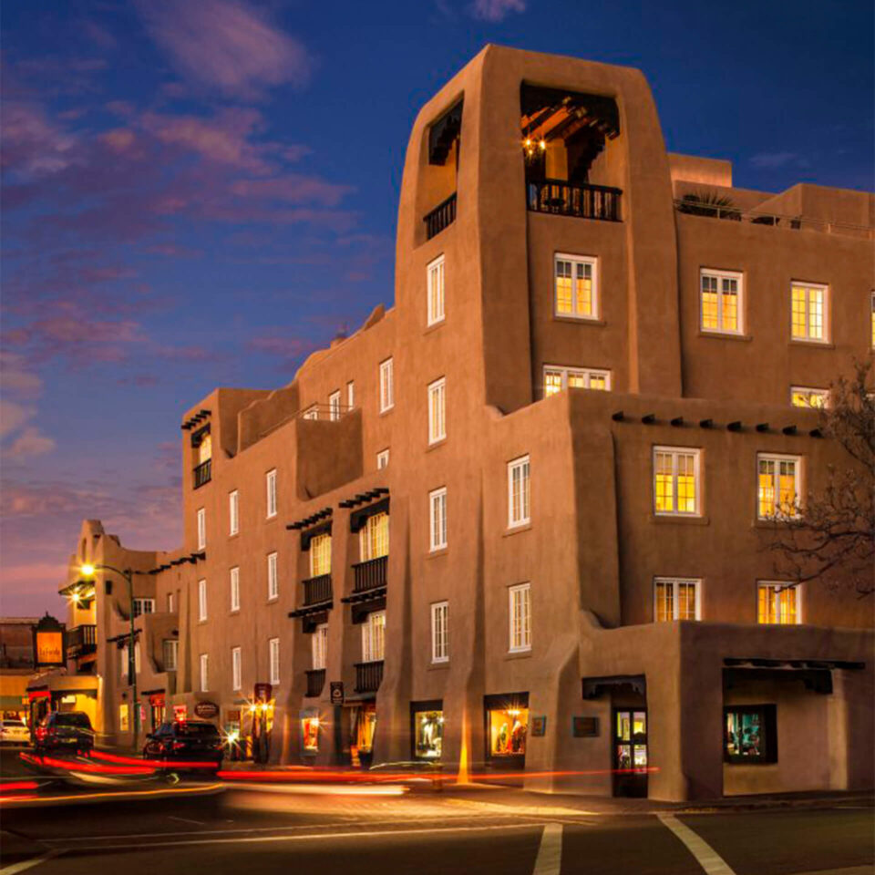 The multi-story adobe-style boutique hotel exterior is captured at twilight with warm light spilling from its many.