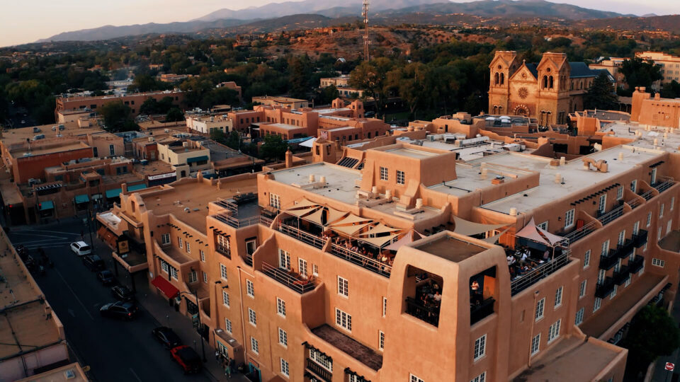 The adobe architecture building features a lively outdoor rooftop bar overlooking the downtown area at sunset.