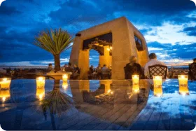 Guests enjoy drinks and dinner on the scenic rooftop bar at twilight, featuring many glowing candles.
