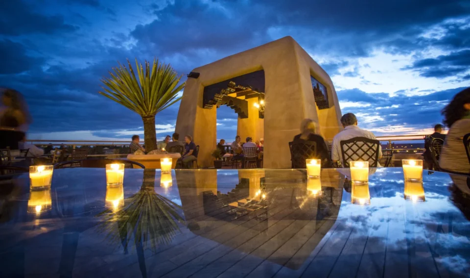 Guests relax at the candlelit rooftop bar, reflecting on the glass table under the dramatic evening sky.