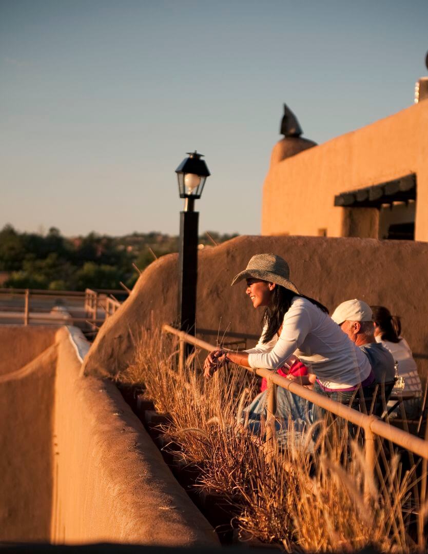 A guest smiles while leaning on the railing overlooking the view from the rooftop bar at sunset.