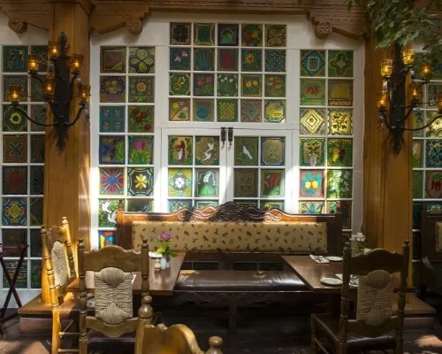 Rustic wooden furniture fills this unique downtown Santa Fe restaurant interior, lit by vibrant, hand-painted window.