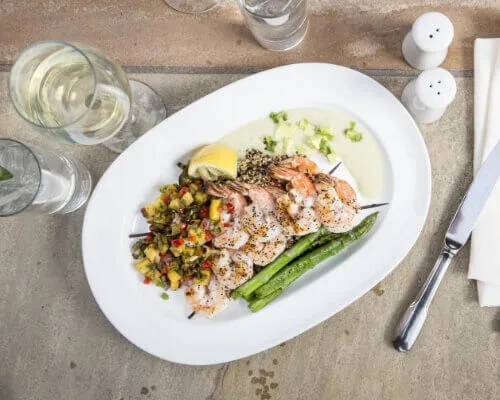A perfectly plated dinner features grilled shrimp on skewers alongside fresh asparagus, quinoa, and colorful salsa.