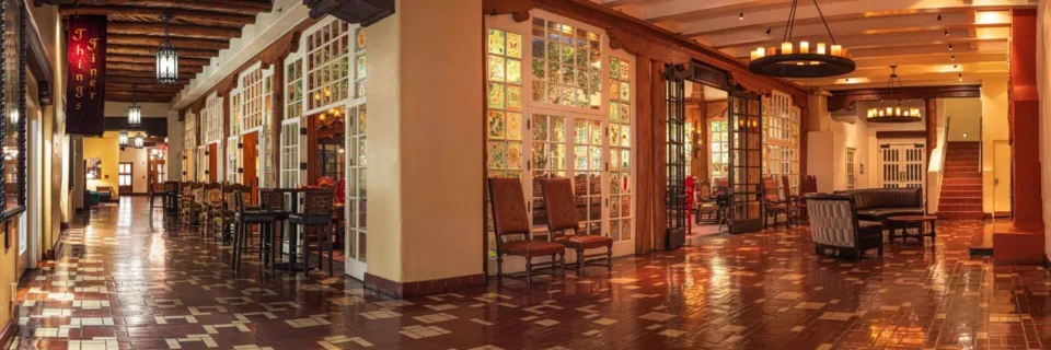 The historic hotel lobby showcases traditional vigas ceilings, tiled floors, and decorative stained glass windows.