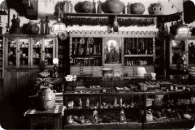 A vintage black and white photograph captures a densely packed display case holding Southwestern pottery, statues, and.