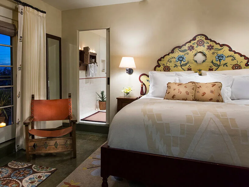 A luxurious Santa Fe hotel room featuring a painted floral headboard and a traditional leather chair.