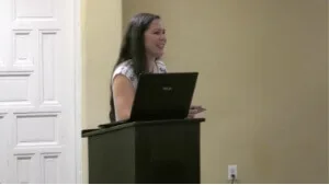 A speaker presents using a laptop on a dark podium within one of the hotel's event spaces.