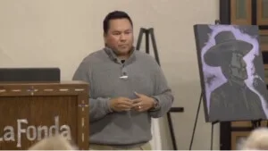 An expert speaker addresses an audience near a painting easel inside a versatile event space.
