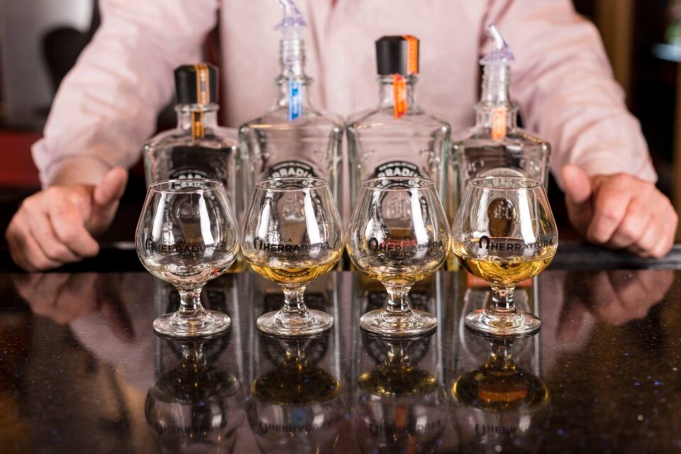 A flight of amber spirits is prepared on a reflective bar counter at the hotel's rooftop bar.