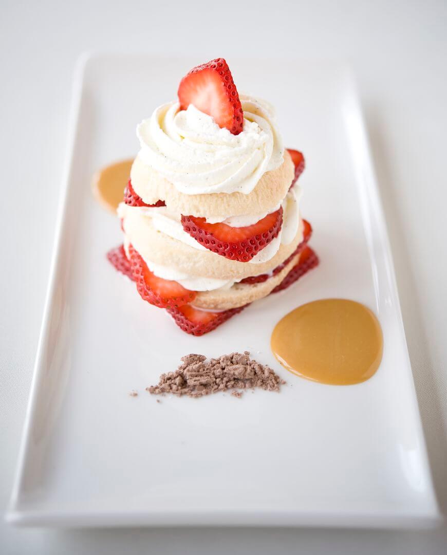 A gourmet stacked strawberry dessert is artfully plated with whipped cream and caramel sauce.